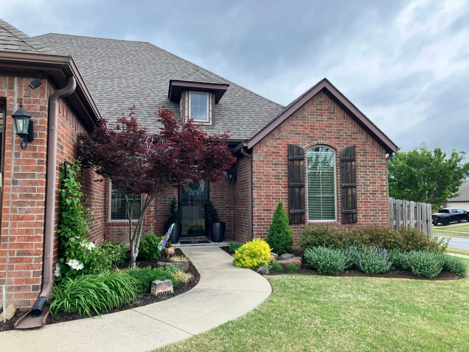 Brick home with a curved front walk, a Japanese maple and freshly planted, mulched front beds