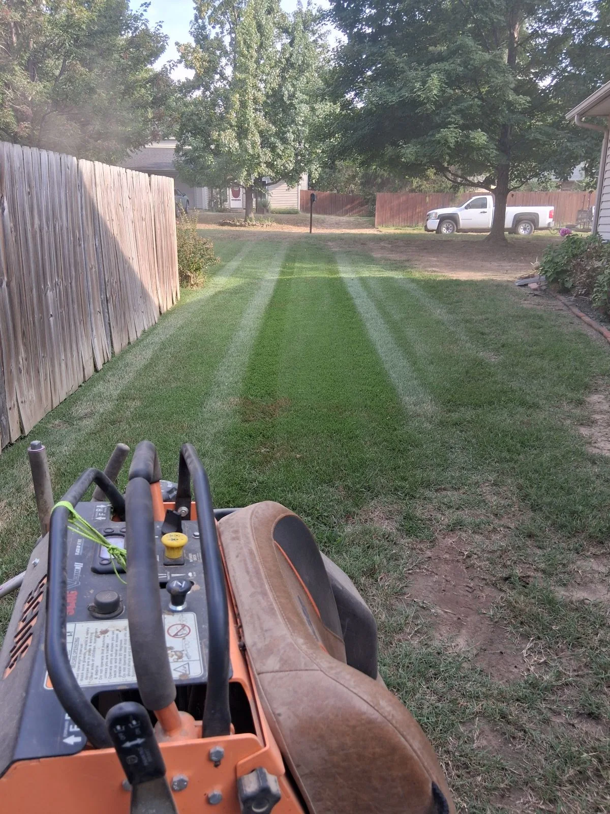 View from a mower across a freshly striped lawn along a wood fence
